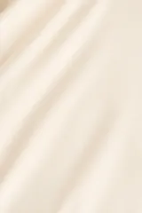 Top de manga larga color beige claro, con escote redondo, hombros caídos y detalle de nudo drapeado en el lateral de la cintura.