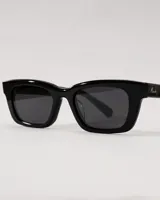 Anteojos de sol negros, montura gruesa y rectangular, con lentes oscuros. Presentan una firma manuscrita en la patilla derecha.