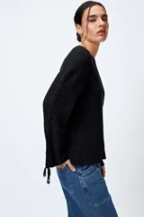 Sweater color crema de tejido de canalé con detalle de trenzado en las mangas y terminación con lazo ajustable.