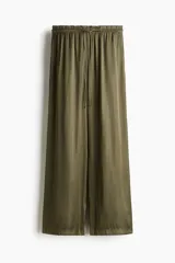Pantalón de corte holgado en tejido fluido de satén verde militar, de piernas amplias, con bolsillos laterales discretos y cintura elástica con cordón ajustable y ribete de volado.