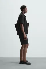 Camisa de corte regular fit confeccionada en tejido con estructura de color negro. Cuenta con cuello bowling, manga corta, aberturas laterales en el bajo y cierre frontal de botones.