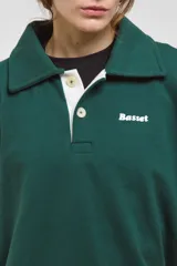 Buzo de algodón en color verde inglés, con diseño de cuello tipo chomba con botones frontales y detalles en blanco. Presenta un corte holgado y cómodo con mangas largas.