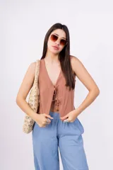 Chaleco corto sin mangas color verde salvia, confeccionado en tela perforada (broderie o calado). Presenta escote en V con lazos ajustables en el centro frontal.