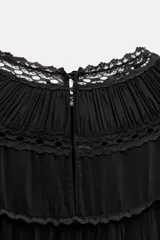 Vestido corto negro con cuello redondo, mangas largas abullonadas con puños elásticos y detalle de encaje y bordados con abalorios. Incluye lazo para ajustar en la cintura.