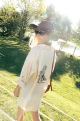 Túnica camisera de lino color beige, de corte largo y holgado, con mangas largas y bordado en la espalda con motivo de coral y texto.