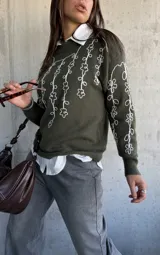 Sweater de punto color verde oliva con cuello redondo y diseño de flores bordadas en hilo blanco en el frente y las mangas.