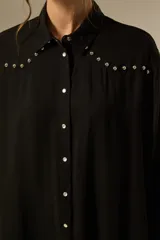 Camisa negra de viscosa con corte holgado, cuello clásico, cierre frontal de botones y detalle de tachas metálicas en la línea de los hombros.