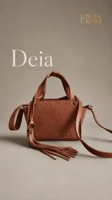 Cartera de mano Lorena Caprile modelo Deia, confeccionada en cuero vacuno con textura grabada. Presenta dos manijas cortas, correa larga ajustable y removible, y detalle de flecos laterales con argolla metálica. Incluye logo grabado en el frente.