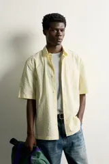 Camisa de corte regular fit color amarillo con rayas verticales blancas, cuello solapa, manga corta, bolsillo de parche en el pecho y cierre frontal con botones.