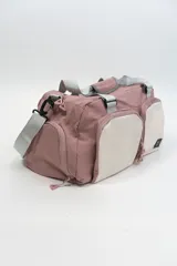 Bolso deportivo color rosa con detalles en beige y gris. Tiene doble asa de mano y correa de hombro ajustable. Cuenta con dos bolsillos frontales con cierre y logo de la marca en la esquina inferior derecha.