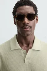 Polo de manga corta color verde azulado oscuro, confeccionado en tejido de punto con textura. Presenta cuello solapa y cierre frontal de botonadura.