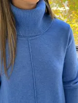 Sweater de punto color azul, con cuello alto acanalado, mangas largas y diseño holgado con costuras verticales decorativas.