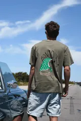 Remera color verde militar de manga corta con estampa en la espalda de un perro caniche con pañuelo de lunares, collar de perlas y gafas de sol, con la inscripción "Bonjour".