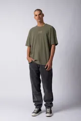 Remera de corte oversize color marrón, con cuello redondo y mangas cortas con hombros caídos. Presenta un bordado minimalista de un joystick en el centro del pecho y una etiqueta aplicada en la parte superior de la espalda.