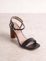 Sandalia de cuero color tostado, con taco alto ancho símil madera y tira ancha en la parte delantera. Presenta doble tira ajustable con hebilla en el tobillo.