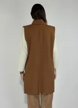 Chaleco largo color beige, con cuello solapa, un botón frontal y dos bolsillos de parche. Presenta costuras decorativas en contraste.