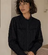 Camisa de broderie negra con detalles calados, cuello alto con volado, mangas largas con puños y cierre frontal de botones.