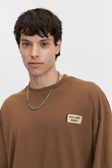 Remera marrón de manga corta con corte boxy, hombros caídos y escote redondo. Presenta un logo estampado en el pecho que dice "GALLERY DEPT.".
