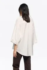 Camisa de manga 3/4 con cuello camisero, silueta ancha y bolsillo de plastrón en el pecho. Presenta un estampado de cuadros en tonos rosado y negro.