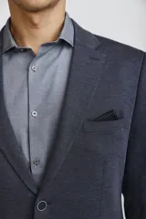 Blazer de corte clásico color azul oscuro, con cierre frontal de un botón, solapas de muesca y bolsillos laterales con solapa. Presenta un bolsillo superior con pañuelo decorativo y puños con botones.
