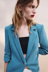 Blazer negro de cuello con solapas de muesca y hombreras, con mangas tres cuartos drapeadas, bolsillos de vivo simulados y cierre frontal con un botón dorado. Forro interior a tono.