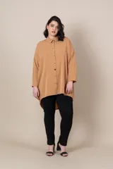 Camisa larga color camel, de corte irregular, más larga en la parte trasera, con botones dorados, manga larga con presilla para sujetar.
