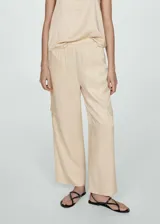Pantalon de corte recto y diseño fluido, confeccionado en tejido satinado color beige. Cuenta con cintura elástica, bolsillos laterales, bolsillos cargo en las piernas y bolsillos de ribete en la parte posterior.