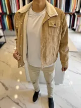 Chaqueta de pana color marrón tostado, con forro interno y cuello de corderito sintético blanco. Presenta cierre frontal de botones metálicos, bolsillos frontales con solapa en el pecho y bolsillos laterales.