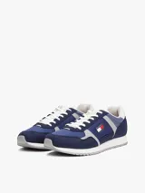 Zapatillas deportivas Tommy Jeans de corte bajo, estilo running, en tonos de azul marino y azul medio, con detalles en gris claro. Presentan una combinación de texturas en el exterior (gamuza, malla y poliéster liso) y cordones blancos. Cuentan con el logo de Tommy Jeans en el lateral.