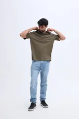Remera oversize verde militar, confeccionada en 100% algodón, con cuello redondo y diseño relajado. Presenta un pequeño bordado frontal en tono naranja.