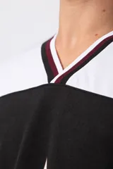 Camiseta de estilo deportivo inspirada en el fútbol americano, con diseño de bloques de color en negro y blanco. Presenta cuello en V con detalles a rayas, mangas cortas anchas y estampado frontal con efecto desgastado que incluye gráficos y texto.