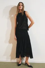 Falda midi negra de tiro medio con superposición de tejido transparente con diseño estampado y aplicación de abalorios a tono. Presenta bajo asimétrico con volantes y forro interior negro.