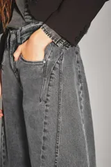 Jean de corte wide leg en color gris oscuro con efecto lavado. Presenta costuras verticales decorativas a lo largo de las piernas y cierre frontal con botón y cremallera.