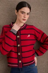 Cardigan de punto con diseño a rayas horizontales en azul marino y beige. Presenta cuello redondo, cierre frontal con botones grandes y mangas largas con puños acanalados en tono verde oliva. Incluye un pequeño bordado de una raqueta de tenis en el lateral.