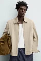 Cazadora color beige de algodón, corte recto, con cuello solapa, cierre frontal con cremallera, manga larga con puños abotonados y bolsillos laterales de ojal.