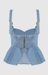 Blusa tipo corset de denim azul claro, con diseño estructurado, escote recto y volado en la cintura. Presenta breteles anchos con detalles de esferas metálicas doradas en la unión con el cuerpo.