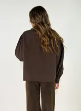 Camisa negra de corte holgado con cuello tipo bebé con volados y lazo de ajuste, cierre frontal con botones y mangas largas abullonadas con puños abotonados.