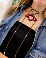 Gargantilla con dije acrílico rojo con incrustaciones de strass y tiras de gamuza marrón con cuentas plateadas.