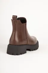 Bota estilo Chelsea de caña baja confeccionada en cuero sintético, con punta redonda, paneles elásticos laterales y suela track dentada de plataforma.