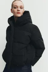 Campera puffer acolchada de color negro, con cuello envolvente, capucha integrada, manga larga, bolsillos laterales ocultos y bajo con elástico. Cierre frontal con botones a presión ocultos por solapa.