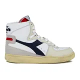 Zapatilla de caña alta Diadora Heritage modelo Mi Basket, color blanco con detalles en azul marino, beige y rojo. Presenta un acabado envejecido en la suela de goma. En la lengüeta se observa un gráfico en blanco y negro de una figura masculina.