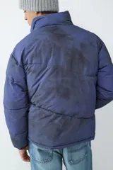 Campera acolchonada con efecto tie-dye en tonos azul y negro, cuello alto, cierre frontal con cremallera y bolsillos laterales. Cuenta con puños elásticos para mayor ajuste.