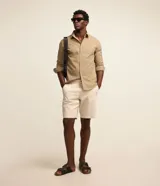 Bermuda masculina slim confeccionada en sarga de algodón con elastano, color beige, con bolsillos laterales tipo chino, bolsillos traseros embutidos con botón, trabillas en la cintura y cierre frontal con botón y cremallera.