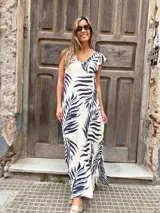 Vestido largo de corte holgado y fluido, con estampado de hojas tropicales en tonos azul marino y celeste sobre base cruda. Cuenta con escote en V y mangas cortas tipo volante.