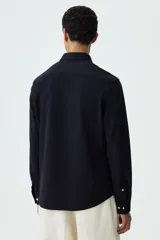 Camisa negra de punto elástico con cuello italiano, cierre frontal de botones y mangas largas.