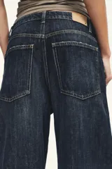 Jeans de tiro medio con diseño baggy barrel, cinco bolsillos y costuras laterales torcidas. Presenta cierre frontal con cremallera y botón metálico.
