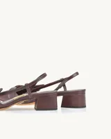 Zapato stileto de cuero color bordeaux, con punta fina, detalle de lazo en el empeine, talón descubierto y tira fina con hebilla.