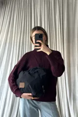 Cartera de mano tipo bolso, color negro, confeccionada en material textil ligero con cierre superior y parche de cuero sintético con logo grabado en el frente.