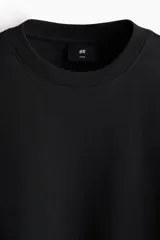 Remera negra de corte oversized y silueta holgada, confeccionada en punto liviano de algodón, con cuello redondo ribeteado y mangas cortas de hombros caídos.