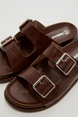 Sandalias planas de mujer con doble tira ancha en el empeine, hebillas metálicas plateadas y textura símil cocodrilo.